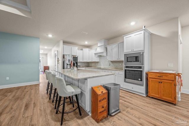 kitchen with stainless steel appliances, premium range hood, backsplash, and light wood-style flooring