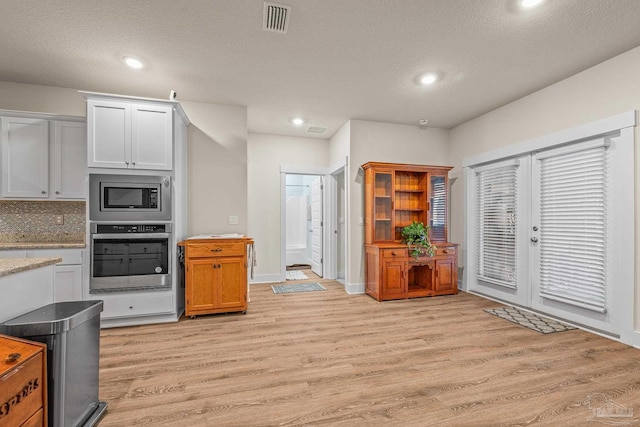 kitchen with a textured ceiling, stainless steel appliances, light wood-type flooring, and visible vents