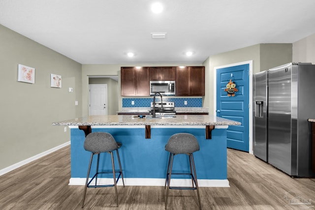 kitchen with appliances with stainless steel finishes, light wood-type flooring, sink, and an island with sink