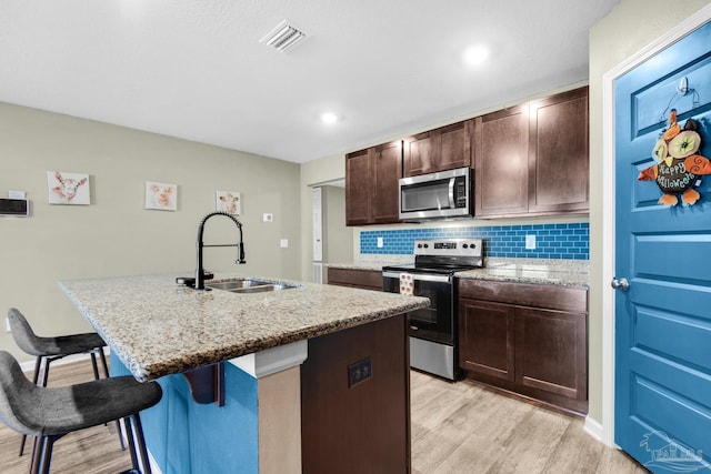 kitchen featuring sink, a kitchen island with sink, light hardwood / wood-style flooring, appliances with stainless steel finishes, and a kitchen breakfast bar