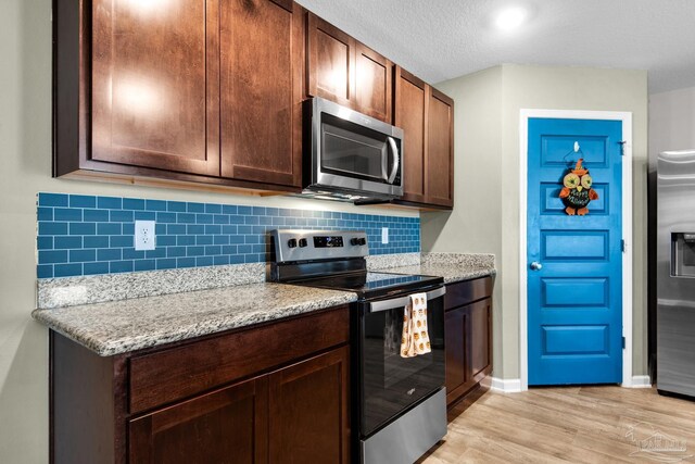 kitchen with light stone countertops, a textured ceiling, appliances with stainless steel finishes, and light wood-type flooring