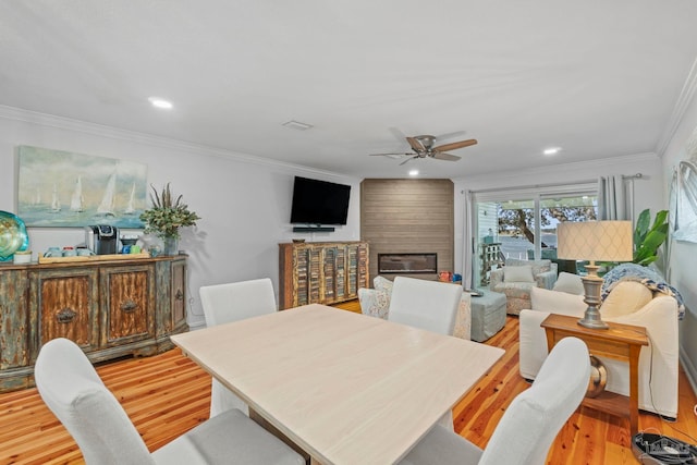 dining room featuring ornamental molding, recessed lighting, a large fireplace, and light wood finished floors