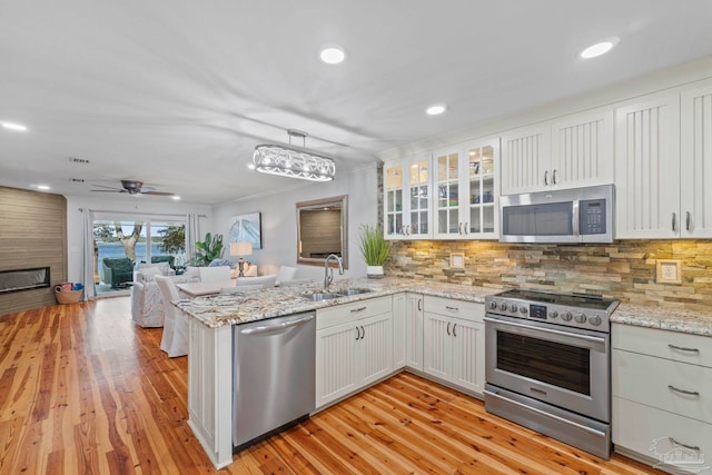 kitchen with stainless steel appliances, open floor plan, a sink, light wood-type flooring, and a peninsula