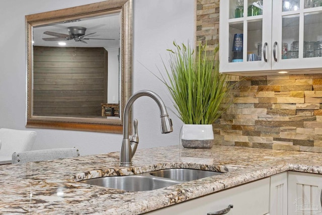 kitchen with tasteful backsplash, glass insert cabinets, light stone counters, white cabinetry, and a sink