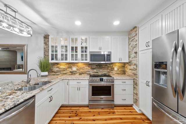 kitchen with stainless steel appliances, backsplash, light wood-style floors, white cabinetry, and a sink