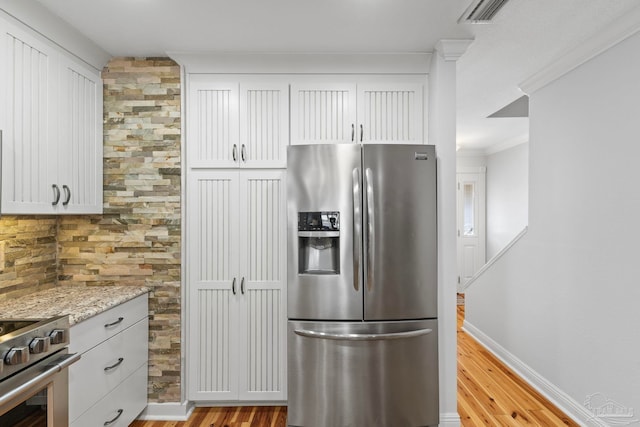 kitchen featuring light wood-type flooring, light stone countertops, ornamental molding, and stainless steel appliances