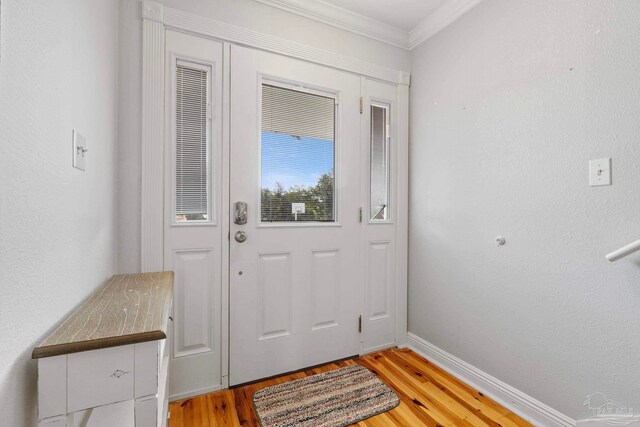 doorway to outside featuring baseboards, a textured wall, ornamental molding, and light wood-style floors