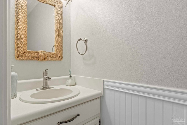 bathroom featuring a wainscoted wall, a textured wall, and vanity