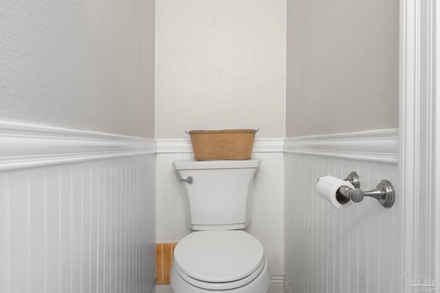 bathroom featuring toilet, a textured wall, and wainscoting