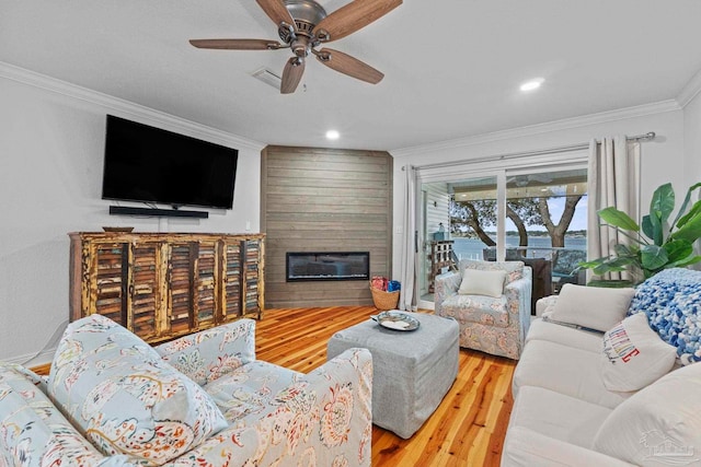 living room featuring a large fireplace, wood finished floors, a ceiling fan, visible vents, and crown molding