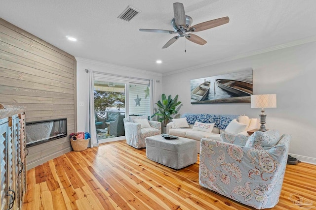 living room with a large fireplace, visible vents, crown molding, and wood-type flooring