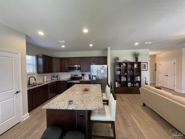 kitchen featuring dark brown cabinets, a sink, a kitchen breakfast bar, stainless steel appliances, and light wood-type flooring