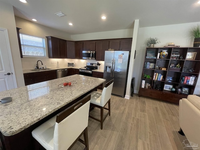 kitchen with dark brown cabinetry, visible vents, appliances with stainless steel finishes, a sink, and a breakfast bar