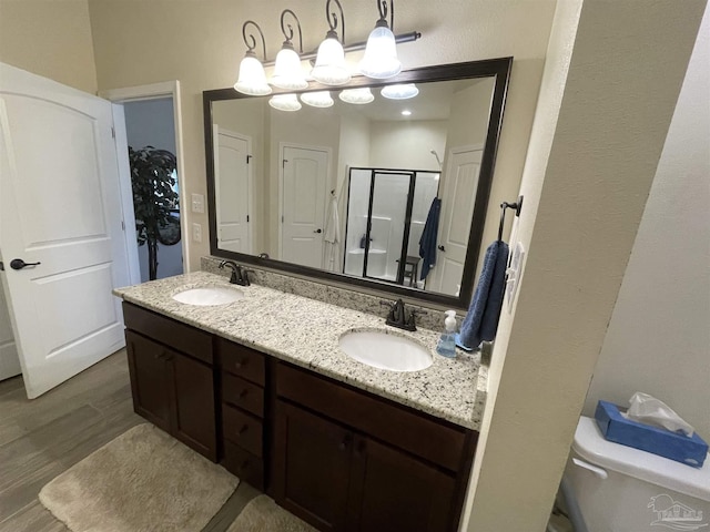 bathroom with wood finished floors, double vanity, a sink, and a stall shower