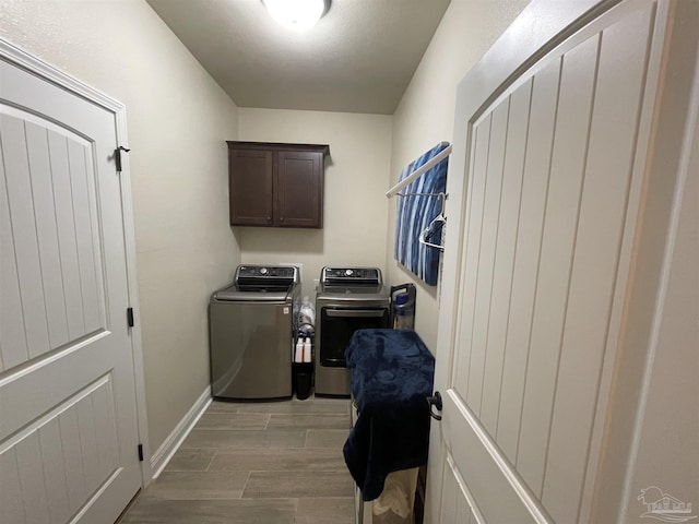 clothes washing area with washing machine and clothes dryer, baseboards, cabinet space, and light wood-style floors