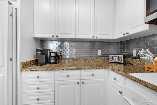 kitchen featuring dark stone countertops, white cabinets, and backsplash