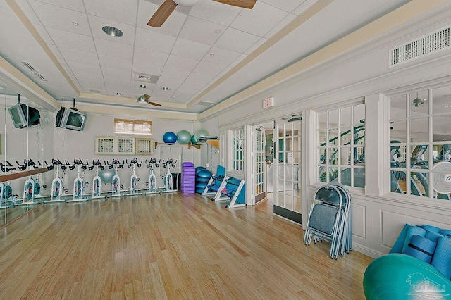 gym featuring hardwood / wood-style flooring, a raised ceiling, and ceiling fan