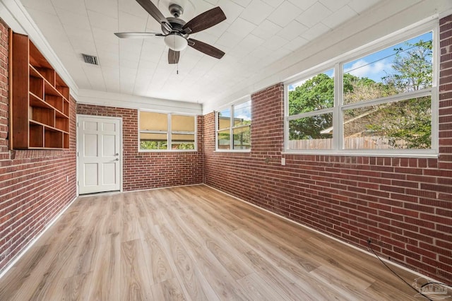 unfurnished sunroom featuring visible vents, a ceiling fan, wood finished floors, and brick wall