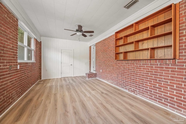 interior space featuring a ceiling fan, brick wall, visible vents, and wood finished floors