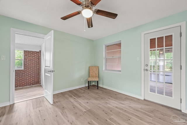 unfurnished room featuring light wood-style floors, baseboards, ceiling fan, and brick wall