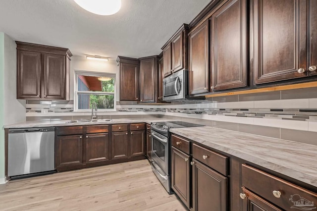 kitchen with appliances with stainless steel finishes, decorative backsplash, a sink, and light wood-type flooring