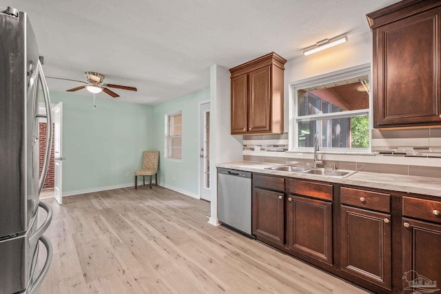 kitchen featuring decorative backsplash, a ceiling fan, light wood-type flooring, a sink, and stainless steel appliances