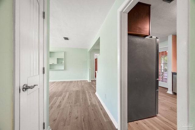 hall featuring baseboards, visible vents, and light wood-style floors