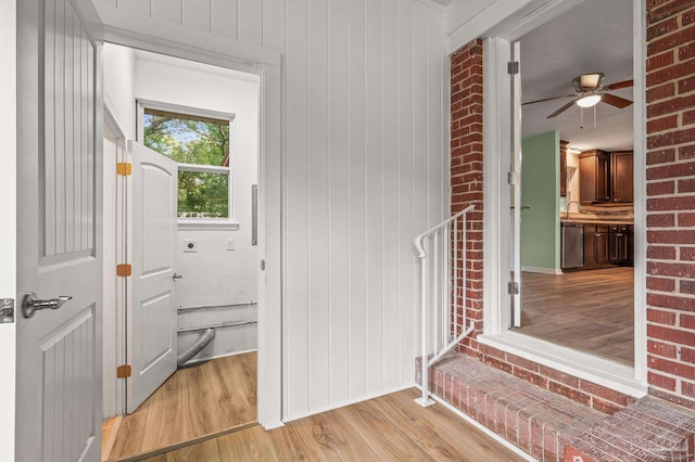 doorway to outside with a sink, wood walls, ceiling fan, and light wood finished floors