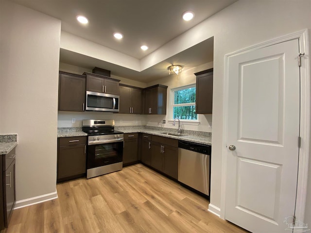 kitchen with light stone counters, stainless steel appliances, light wood-type flooring, dark brown cabinets, and sink