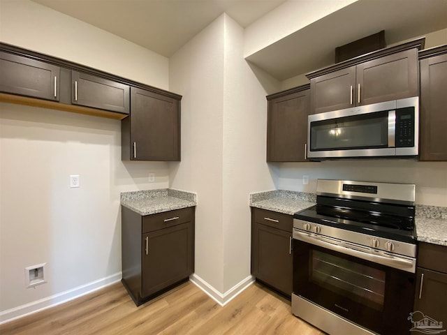 kitchen with light hardwood / wood-style floors, dark brown cabinets, light stone counters, and appliances with stainless steel finishes