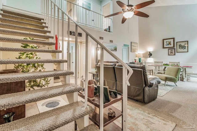 living room with a towering ceiling, ceiling fan, and carpet floors