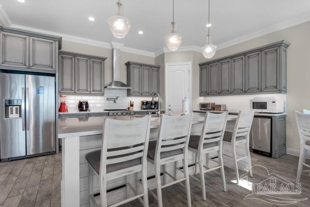 kitchen featuring tasteful backsplash, wall chimney range hood, dark hardwood / wood-style flooring, stainless steel refrigerator with ice dispenser, and a kitchen island with sink