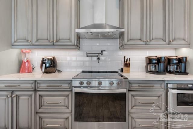 kitchen featuring stainless steel appliances, wood-type flooring, backsplash, and wall chimney exhaust hood