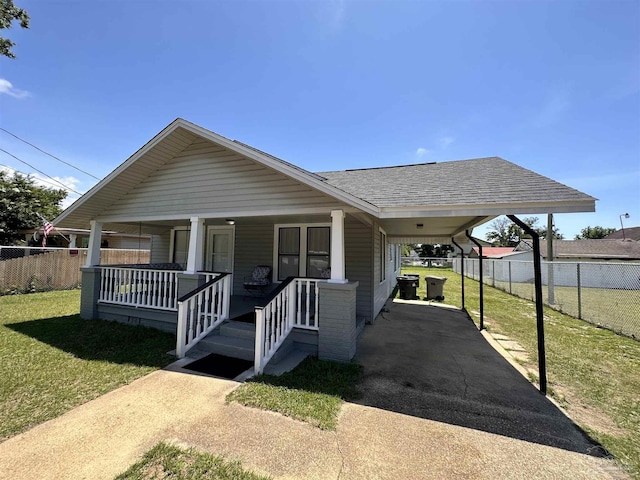 bungalow-style house with an attached carport, covered porch, a shingled roof, driveway, and a front yard