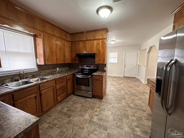 kitchen featuring under cabinet range hood, stainless steel appliances, a sink, backsplash, and brown cabinetry