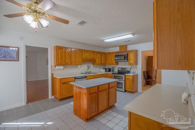 kitchen with ceiling fan, appliances with stainless steel finishes, a kitchen island, a textured ceiling, and sink