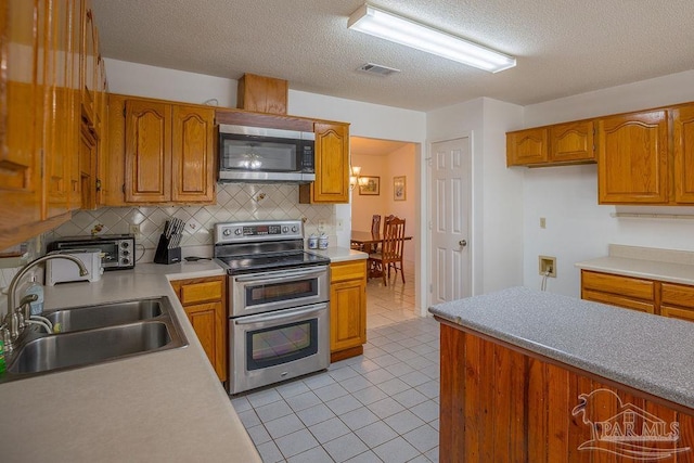 kitchen with sink, light tile patterned flooring, appliances with stainless steel finishes, a textured ceiling, and tasteful backsplash