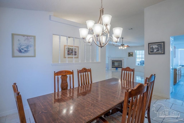 dining area featuring ceiling fan with notable chandelier, vaulted ceiling, light tile patterned floors, and a fireplace