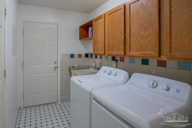 laundry room with sink, light tile patterned floors, tile walls, washing machine and dryer, and cabinets