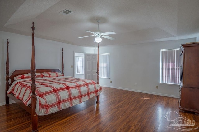 bedroom with dark hardwood / wood-style flooring, a textured ceiling, a raised ceiling, and ceiling fan