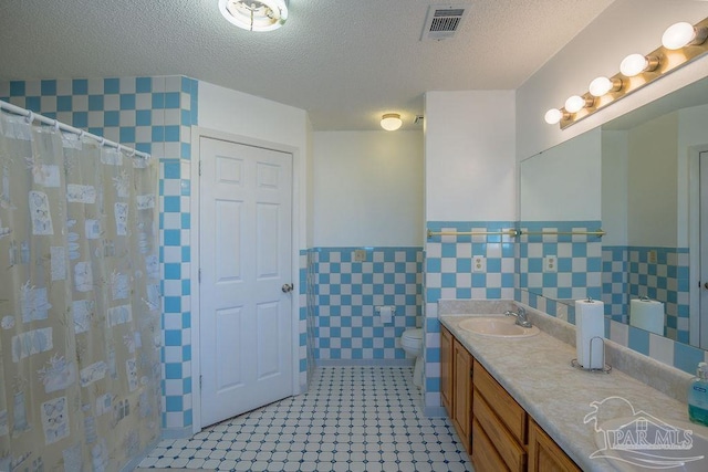 bathroom with toilet, a textured ceiling, vanity, and tile walls