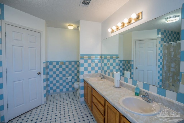 bathroom featuring tile walls, vanity, a textured ceiling, and toilet