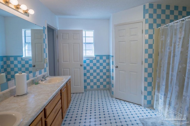 bathroom with tile walls, vanity, a textured ceiling, and walk in shower