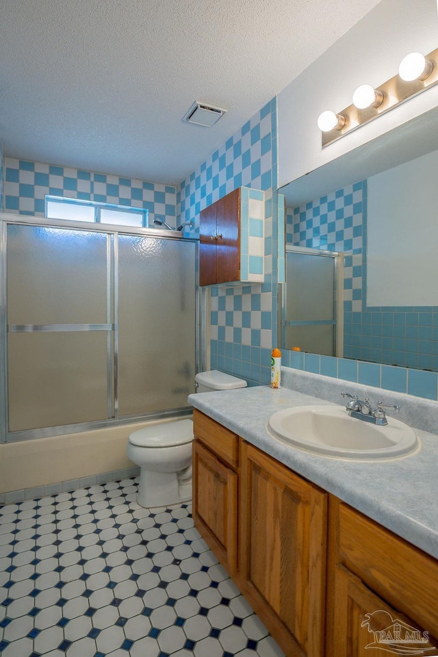 full bathroom with vanity, enclosed tub / shower combo, a textured ceiling, and toilet