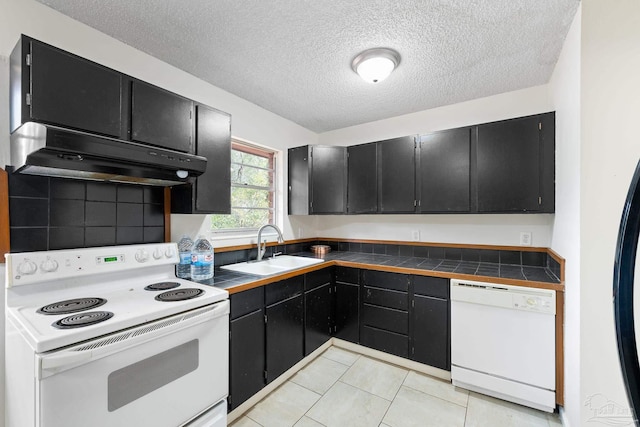 kitchen featuring sink, white appliances, tile counters, a textured ceiling, and light tile patterned flooring