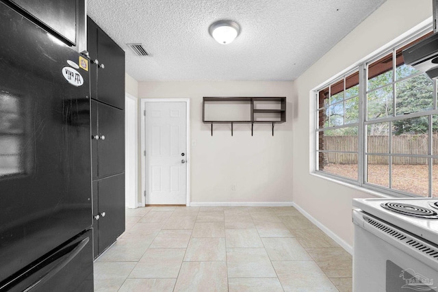 kitchen featuring light tile patterned floors, black refrigerator, white range with electric stovetop, a textured ceiling, and exhaust hood