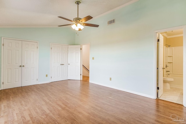 unfurnished bedroom featuring vaulted ceiling, ceiling fan, crown molding, connected bathroom, and multiple closets