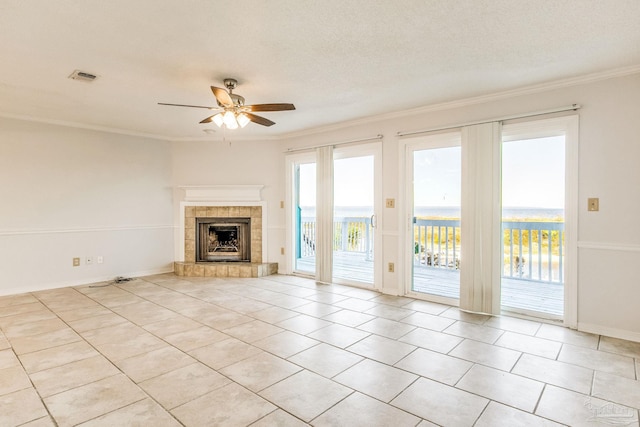 unfurnished living room featuring ceiling fan, ornamental molding, a textured ceiling, and a tiled fireplace