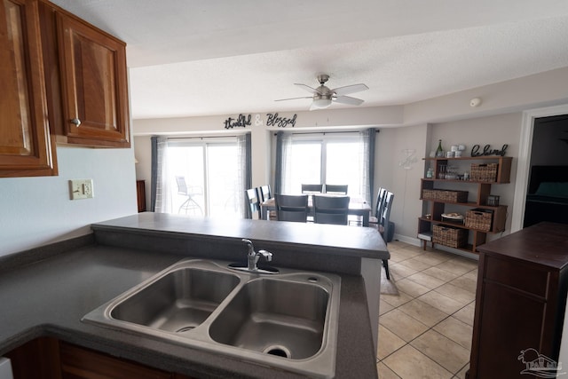 kitchen featuring light tile patterned floors, ceiling fan, a sink, a peninsula, and dark countertops