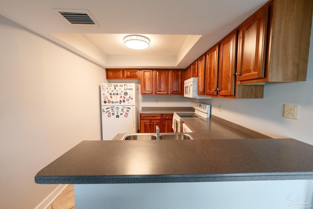 kitchen featuring a peninsula, dark countertops, visible vents, a raised ceiling, and white appliances